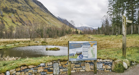 Visitor signage in a stone circle with green and snow-capped hills behind.