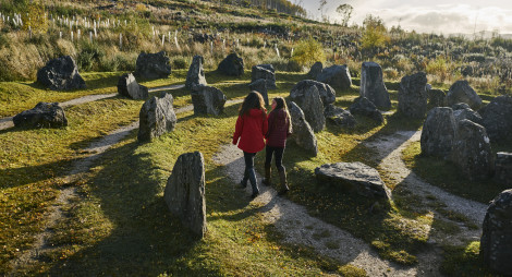 Rear view of woman in red jacket and teenage girl walking through Touchstone Maze, labyrinth of Scottish stones, Blackmuir Wood, near Strathpeffer