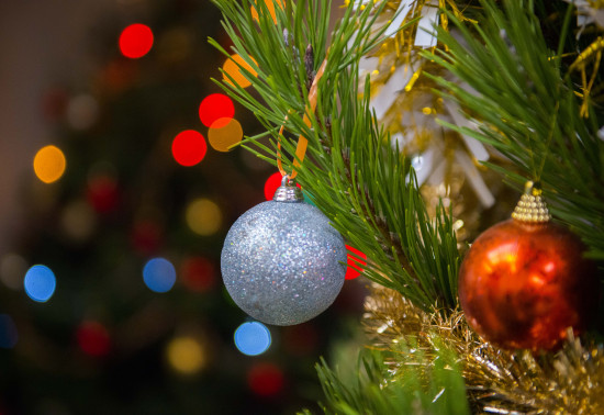 Close up of a sparkly blue Christmas bauble hanging from a Christmas tree. There are colourful lights in the background. 
