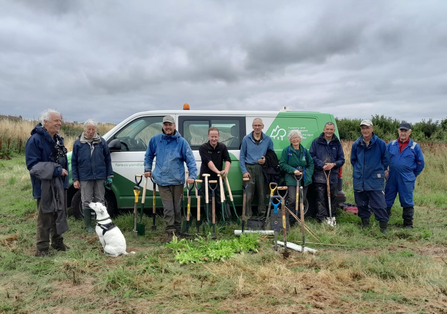 A team of FLS staff and volunteers standing in a meadow in front of a branded work van