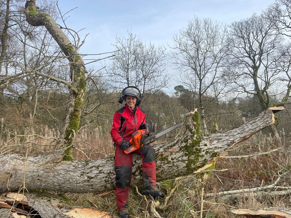 woman sitting on a felled tree with a chain saw