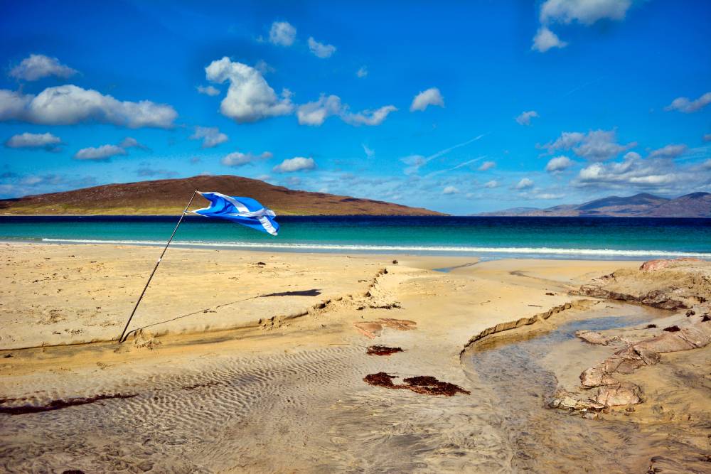View of golden beach, turquoise water and bright blue sky with Scottish saltire flag flying in the breeze