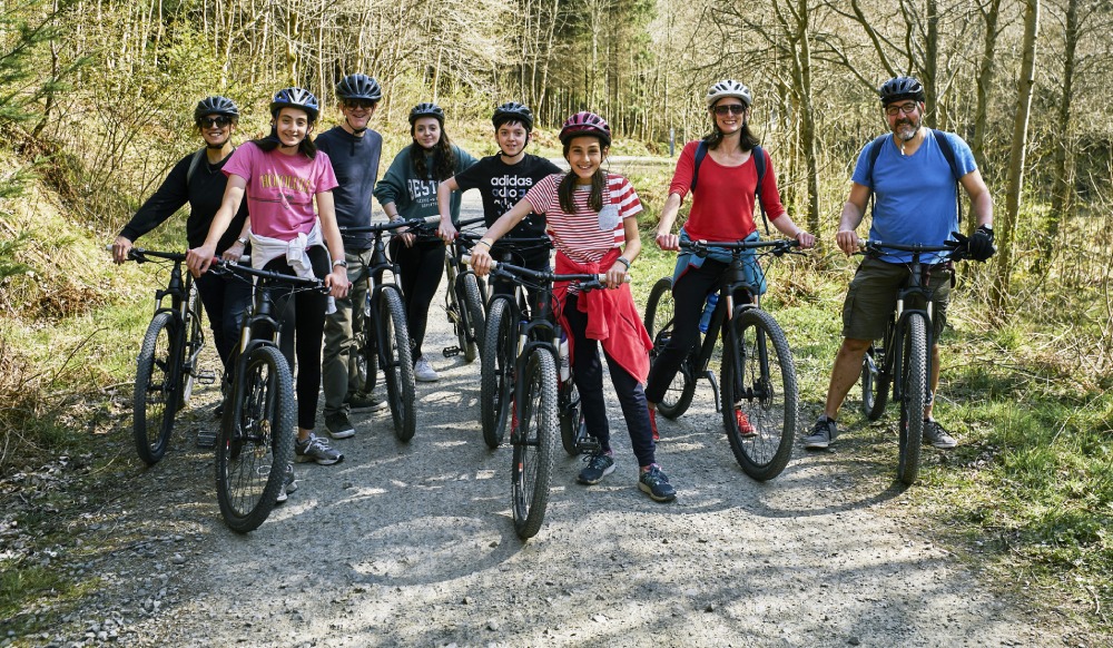 Group of children and adults on mountain bikes stopped on forest road and smiling for the camera