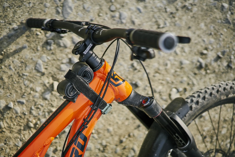 Front of mountain bike showing an orange frame and handlebars, bike leant on the ground, with an inner tube strapped to the frame
