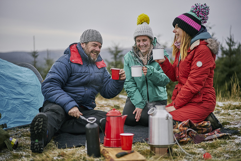 Three people wrapped up in warm clothes outside enjoying a cup of tea
