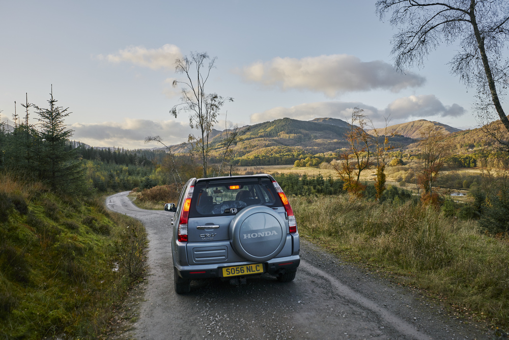 Rear view of car being driven on road, with surrounding Trossachs hills, on Three Lochs Forest Drive, near Aberfoyle
