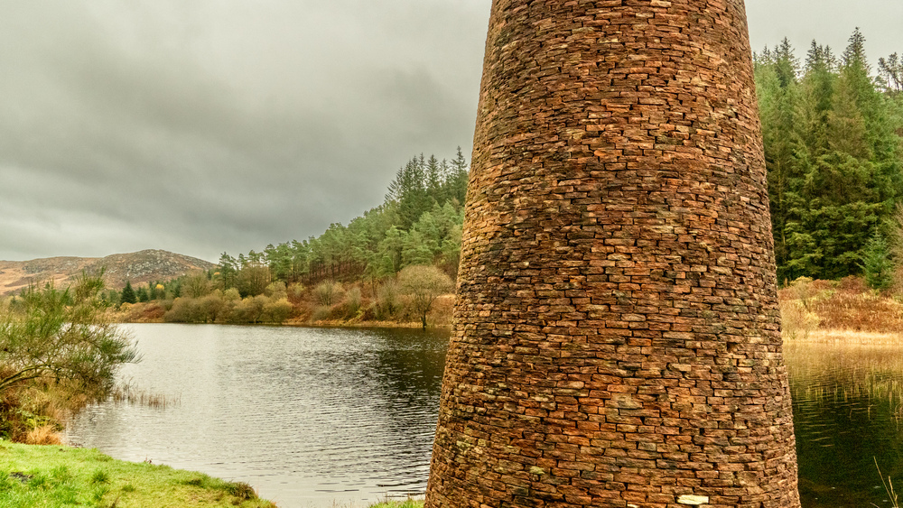 A brick sculpture next to a quiet loch surrounded by conifer trees