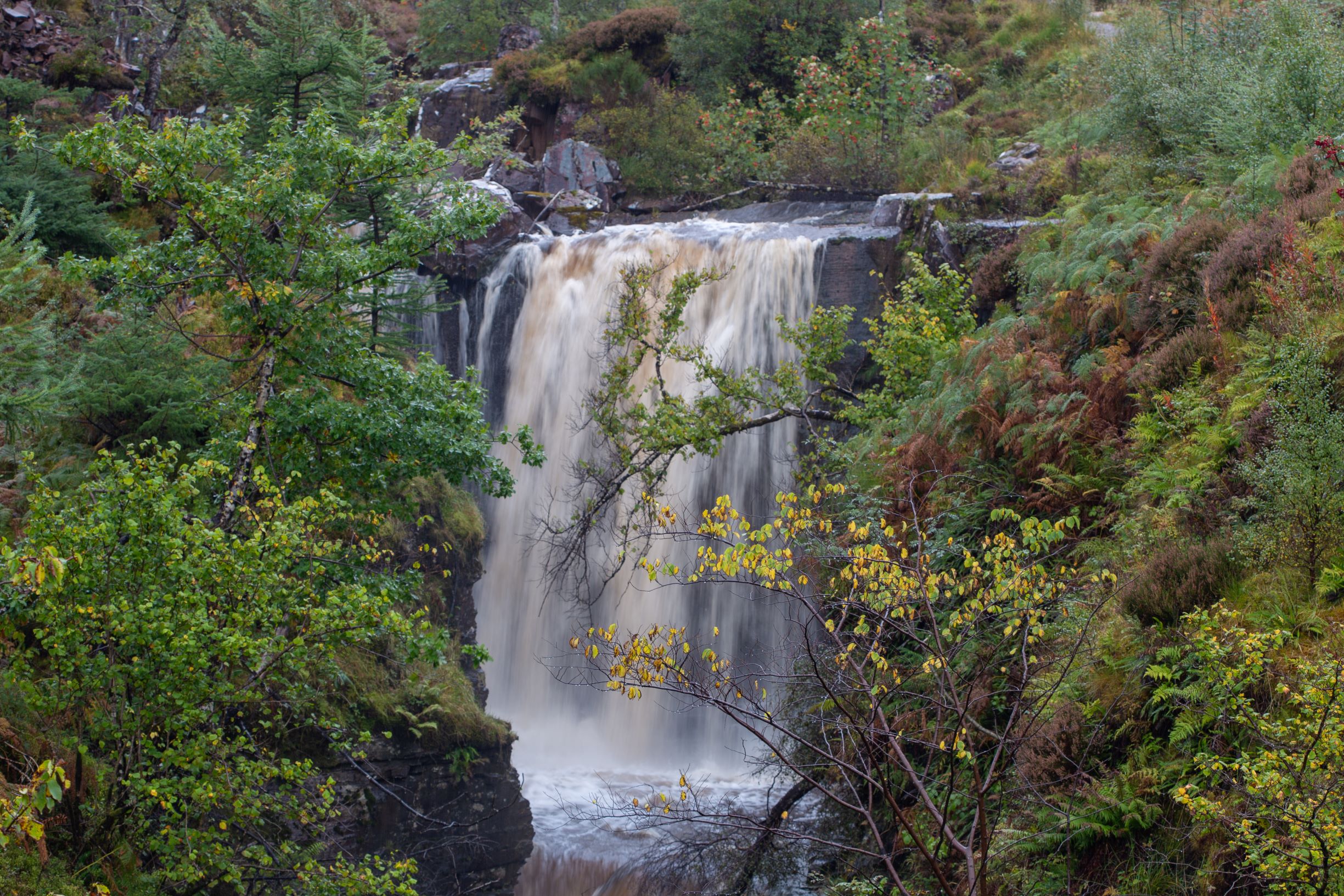 A high waterfall crashing into a river surrounded by trees at Slattadale