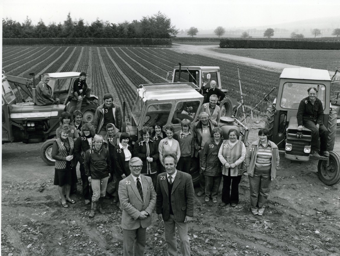 Black and white image of a group of people standing in front of neat fields