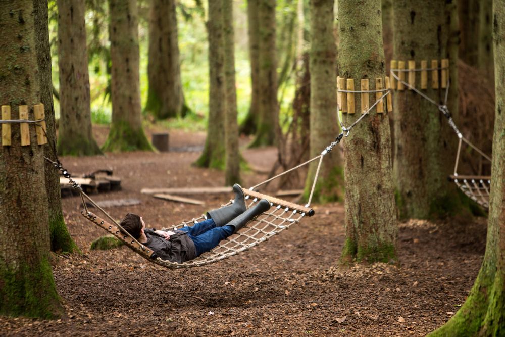 Boy in wellies lying on an rope hammock strung between two trees in a forest