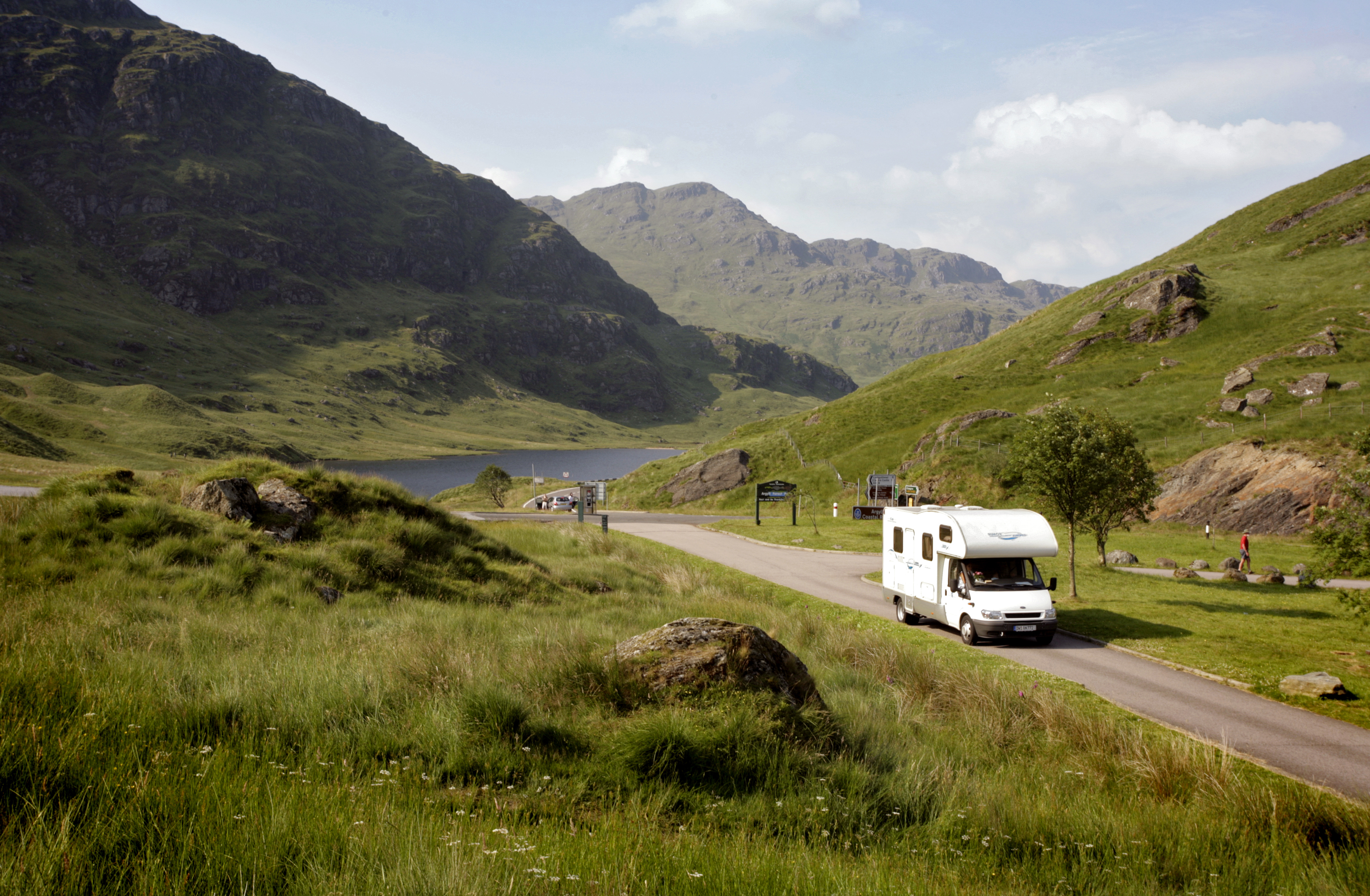Motorhome driving on singletrack road surrounded by lush green hillsides