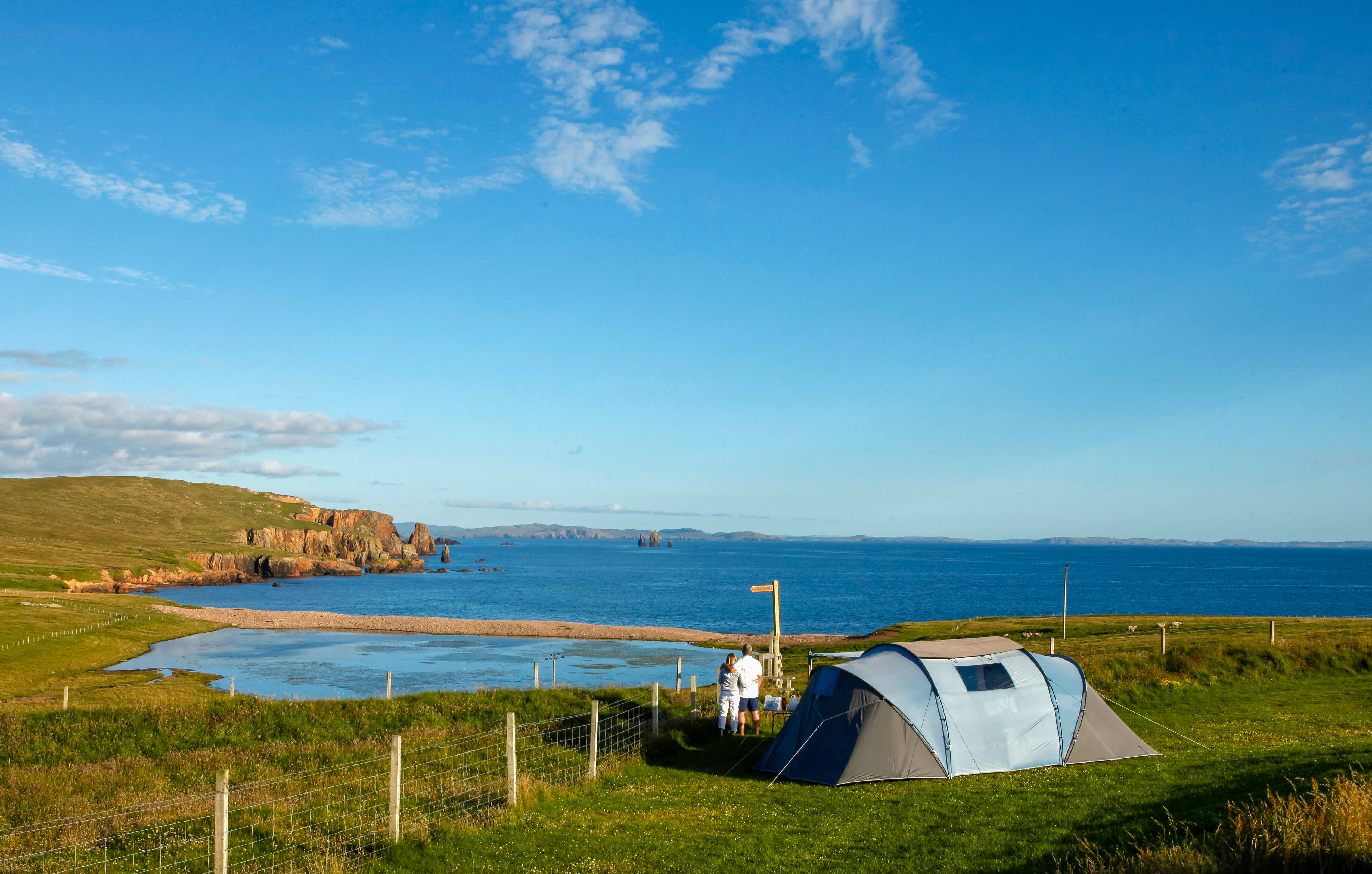 Large tent set in a green field overlooking a dramatic coastline of blue sea and sky