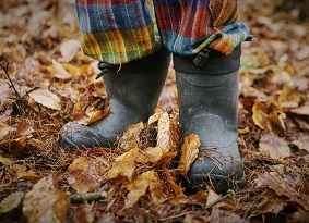 Child in welly boots standing in brown leaves