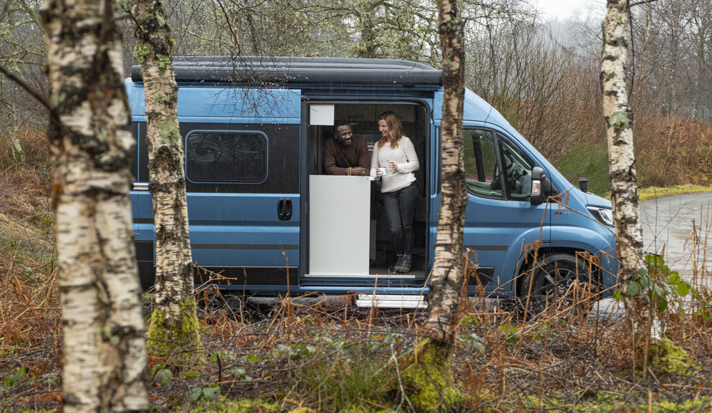  BAME couple drinking coffee/tea in motorhome/campervan with open door, at Leannach Forest car park, Queen Elizabeth Forest Park