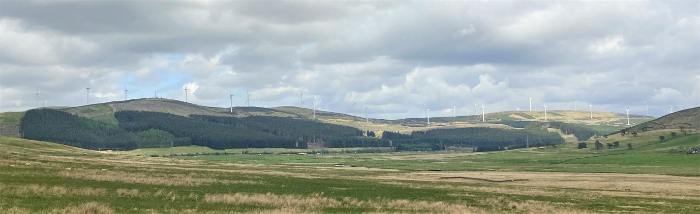 an open area with treed hills and wind turbines