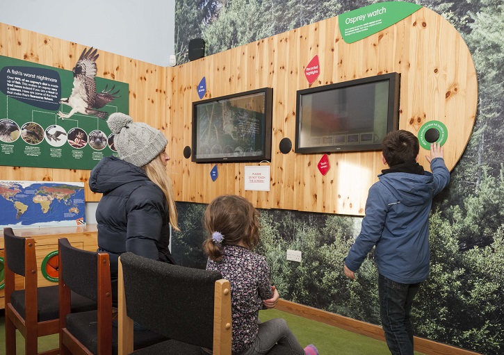 Adult and two children in an interactive visitor centre learning about the workings of a forest