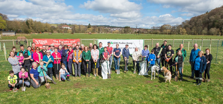 Group of people gathered together in a semi-circle for a photo in a green field with banner behind