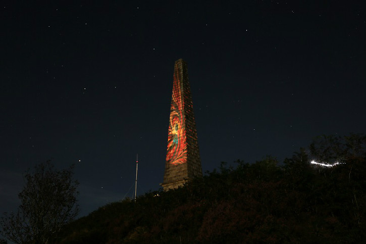 A tall stone monument at night projected with a colourful design in lights