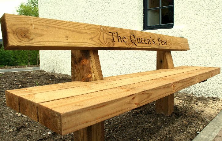 Sturdy wooden outdoor bench with carved words 'The Queen's Pew'