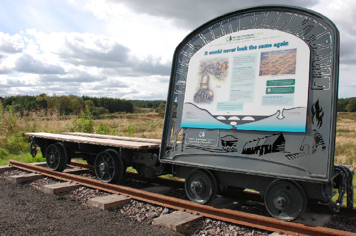 Two vintage flat-bed rail cars on a short railway track, one with an interpretation panel explaining the area
