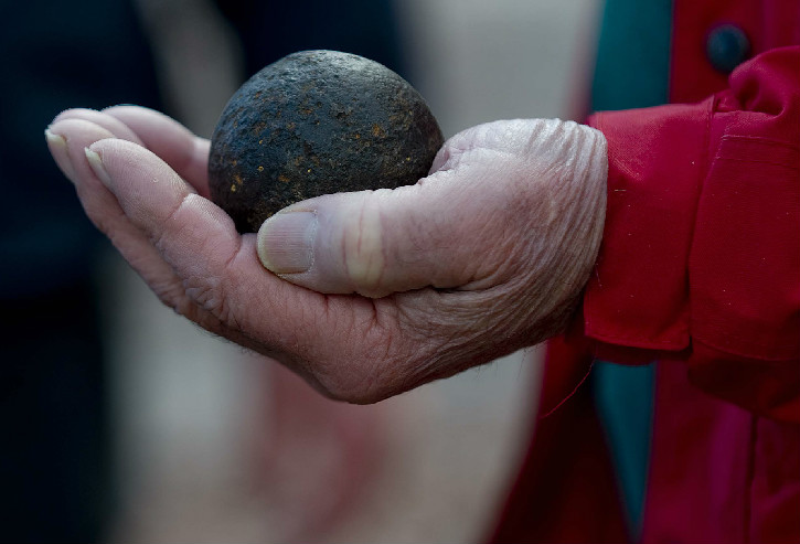 Person's hand holding an antique iron canonball