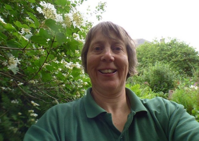 Woman in green t-shirt looking at camera with green trees behind
