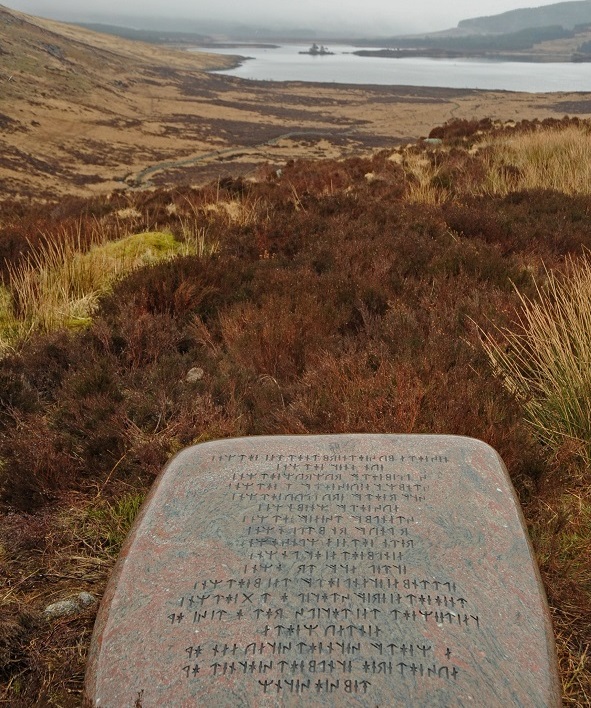 Large polished stones engraved with runes lying in bracken on a hillside above a loch