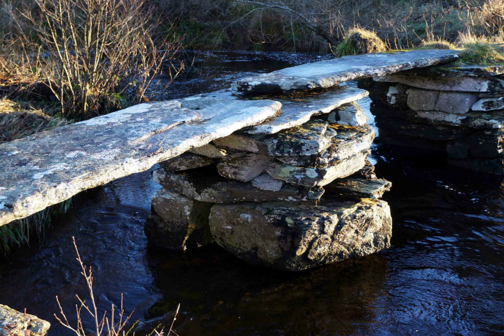 Small footbridge made of large stones crossing dark burn