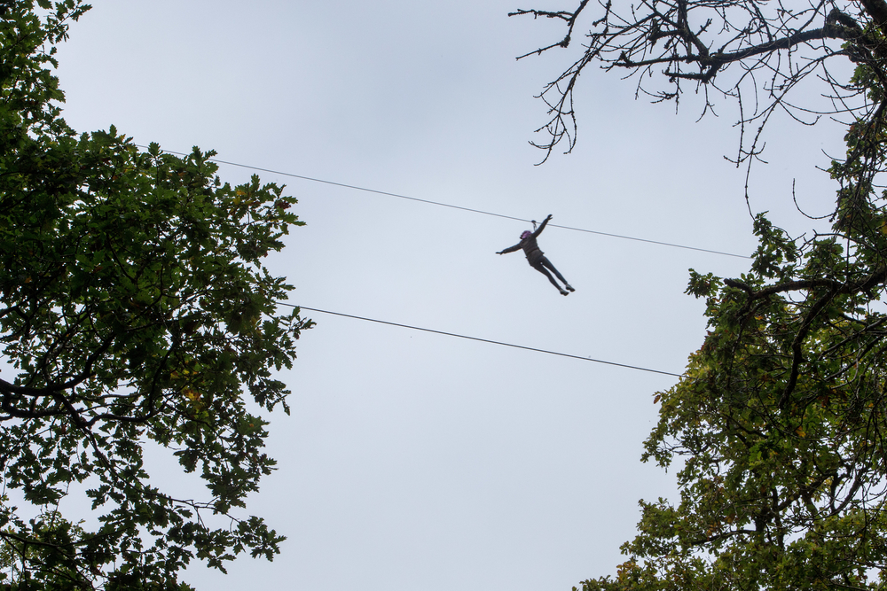 Someone on a zip line at GoApe, with the sky above.