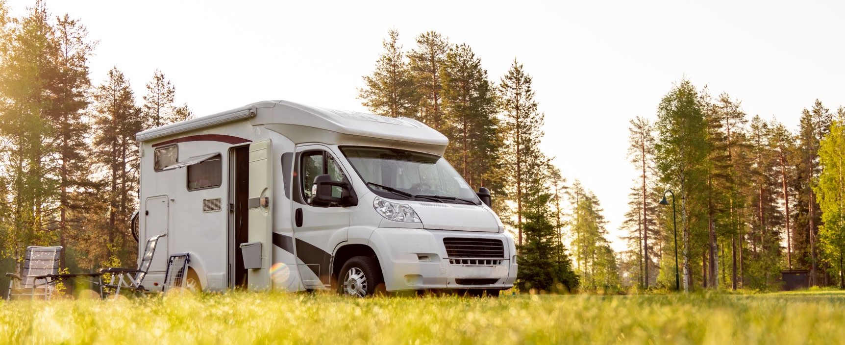 Motorhome parked on a grassy field in golden sunlight with trees behind.