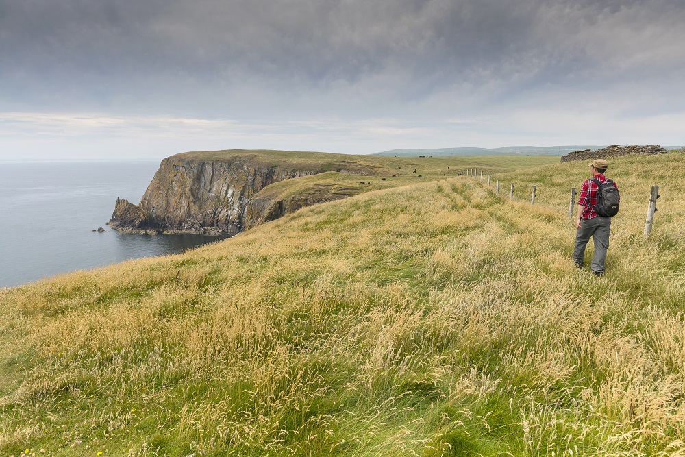 A man walking across grass towards a large coastal cliff face