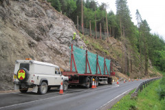 A white jeep and lorry in a forest road with people propelling on the rock face 