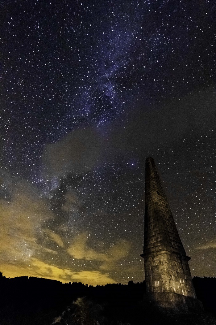 View of the night sky with lots of stars from the ground, with an old, tall stone tower in the foreground