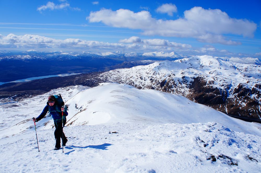 Person walking up a high snow-covered hill with blue skies