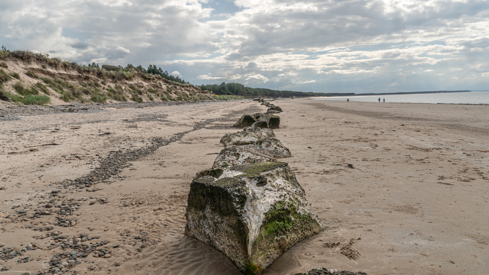Large sandy beach with line of large rocks stretching to horizon