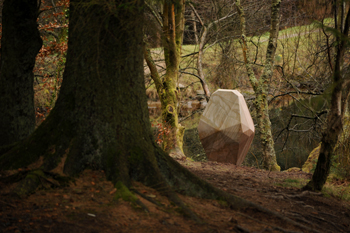 A geometric carved boulder sitting among trees