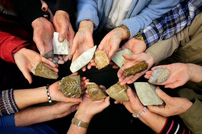Group of hands combining in centre of image each holding different carved stone