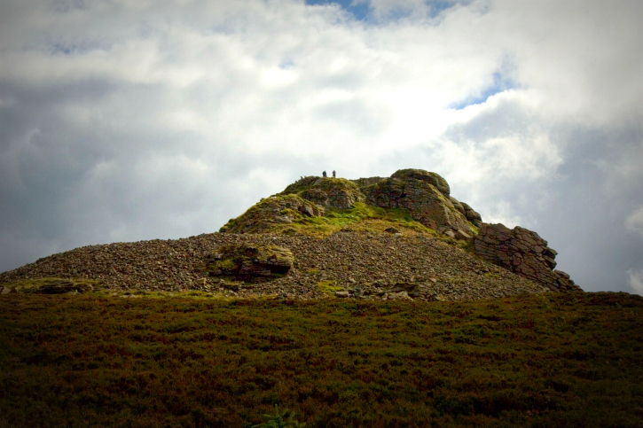 Looking up the summit of a craggy hill with cloudy sky beyond