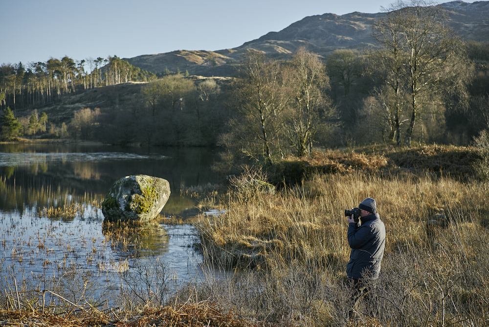 Man near still water taking a picture of surroundings