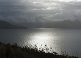 View of sun shining through dark clouds on to the sea