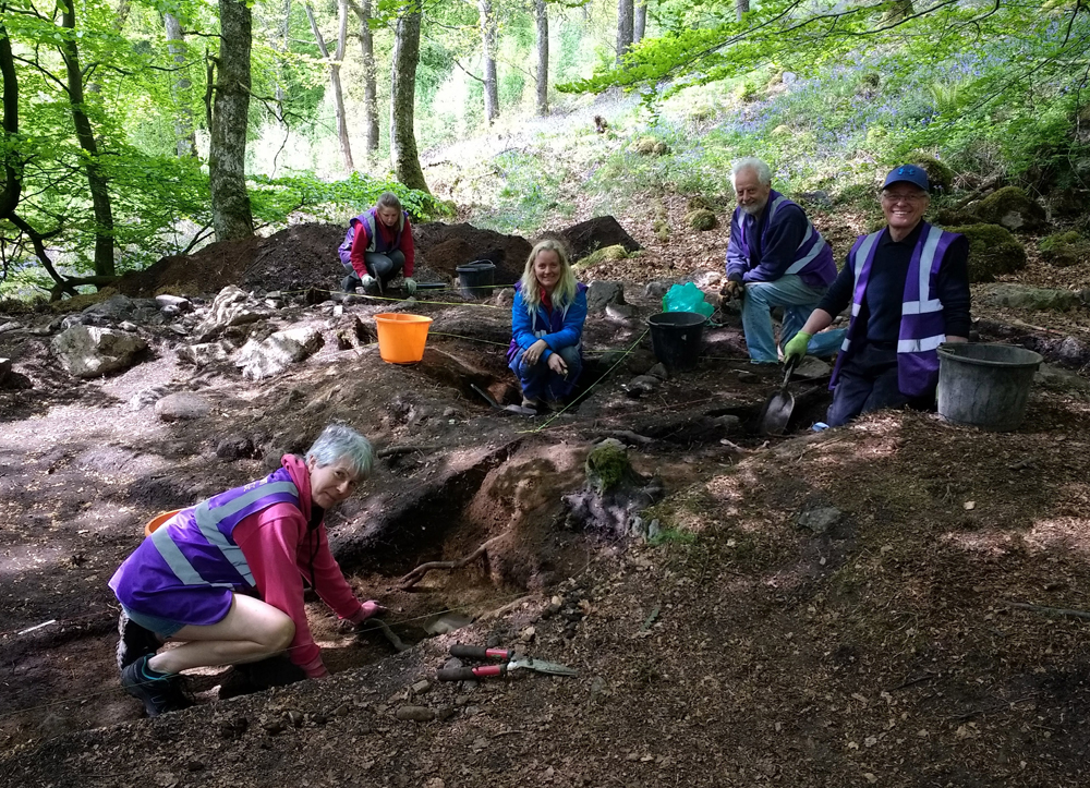 Group of adults clustered around archaeological dig site in forest