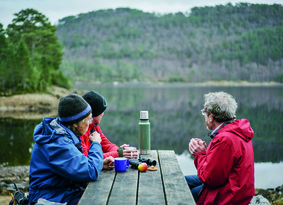 Three people at a picnic bench next to a large loch