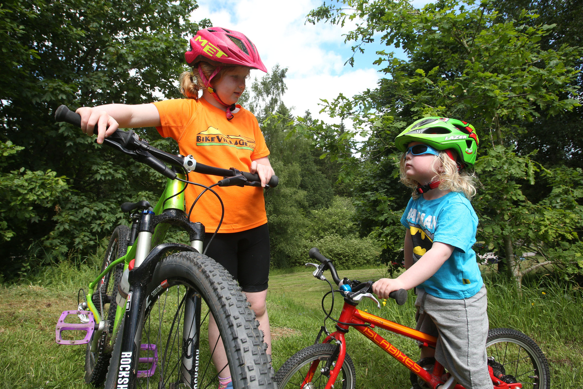 Two young children with bikes on a forest path