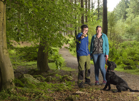 A man, woman and dog standing on a woodland path