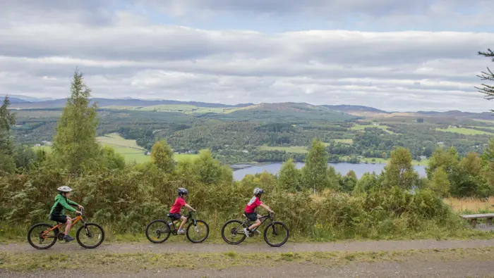 Three mountain bikers in the foreground with a view out to the glen in the background.