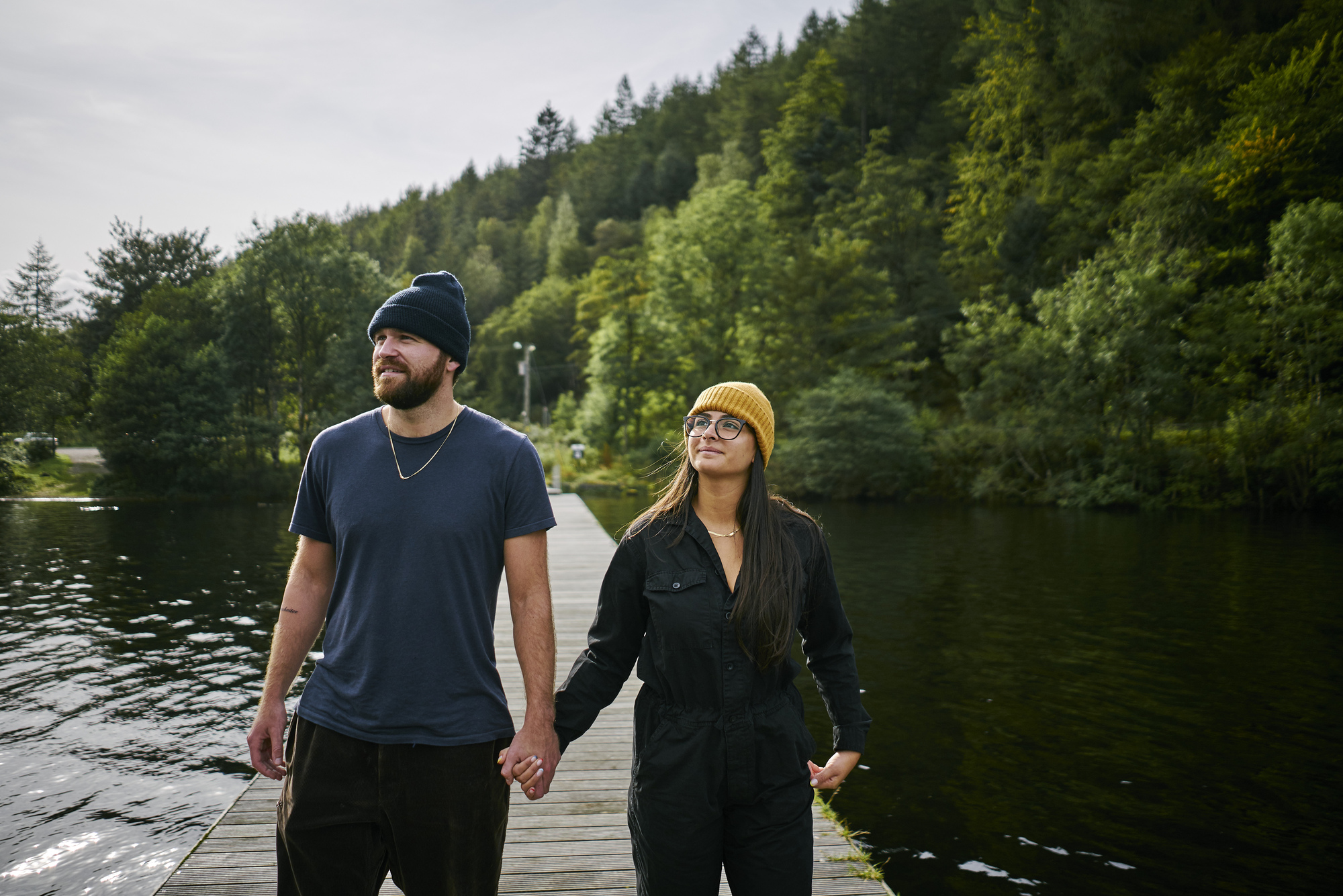 Man and woman walk hand in hand along wooden jetty, protruding into Loch Oich, near Fort William