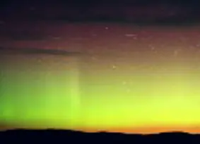 Green, yellow and red aurora borealis above a silhouette of rolling hills