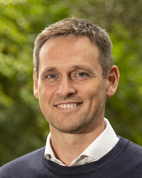 A head shot of a man in front of trees