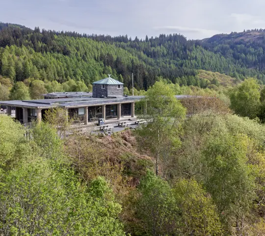 An aerial shot of a building through trees with hills behind