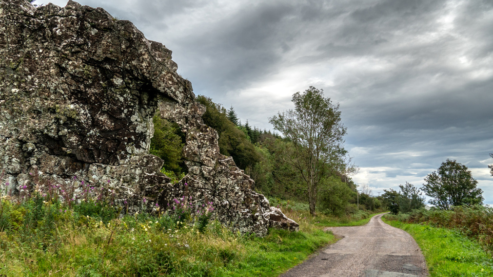 A road next to a large rock formation with a hole in it